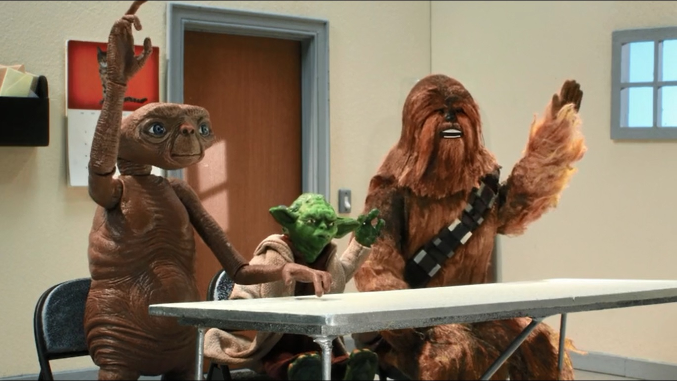 Adegan dari acara TV animasi/stop-motion Robot Chicken (acara yang memparodikan segala sesuatu yang bersifat fiksi ilmiah).  Di sini kita melihat ET (alien kecil berwarna coklat), Yoda (alien hijau yang lebih kecil lagi yang mengenakan jubah), dan Chewbacca (seorang humanoid berbulu besar yang mengenakan bandolier).  Mereka bertiga sedang duduk di depan meja di ruang kelas, masing-masing dengan satu tangan terangkat siap menjawab pertanyaan.