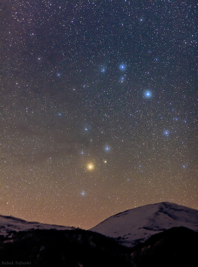 bintang merah terang di tengah deretan bintang di langit malam terlihat di atas beberapa puncak gunung