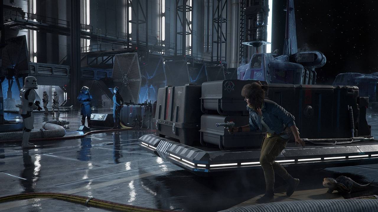 Cuplikan dari video game Penjahat Star Wars.  Di sini kita melihat karakter utama Kay Ves, pistol terhunus, dan makhluk kecilnya, Nix, bersembunyi di balik tumpukan besar kotak kargo di gantungan kapal.  Mereka berusaha menghindari dua orang berseragam hitam di depan mereka.  Kay memiliki rambut sebahu, rambut coklat lebat, dia mengenakan cropped jacket biru, kemeja putih, celana panjang coklat dan ikat pinggang coklat.  Nix adalah makhluk kecil seukuran kucing, dengan 2 mata, 4 kepala ekor, satu ekor berukuran sedang dan bulu halus.