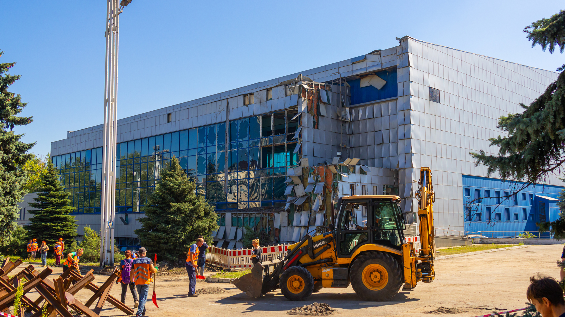 Pekerja dengan sekop dan backhoe membersihkan tanah dan puing-puing di dekat kompleks olahraga yang rusak akibat salah satu rudal Rusia pada 15 Agustus 2023 di Dnipro, Ukraina.