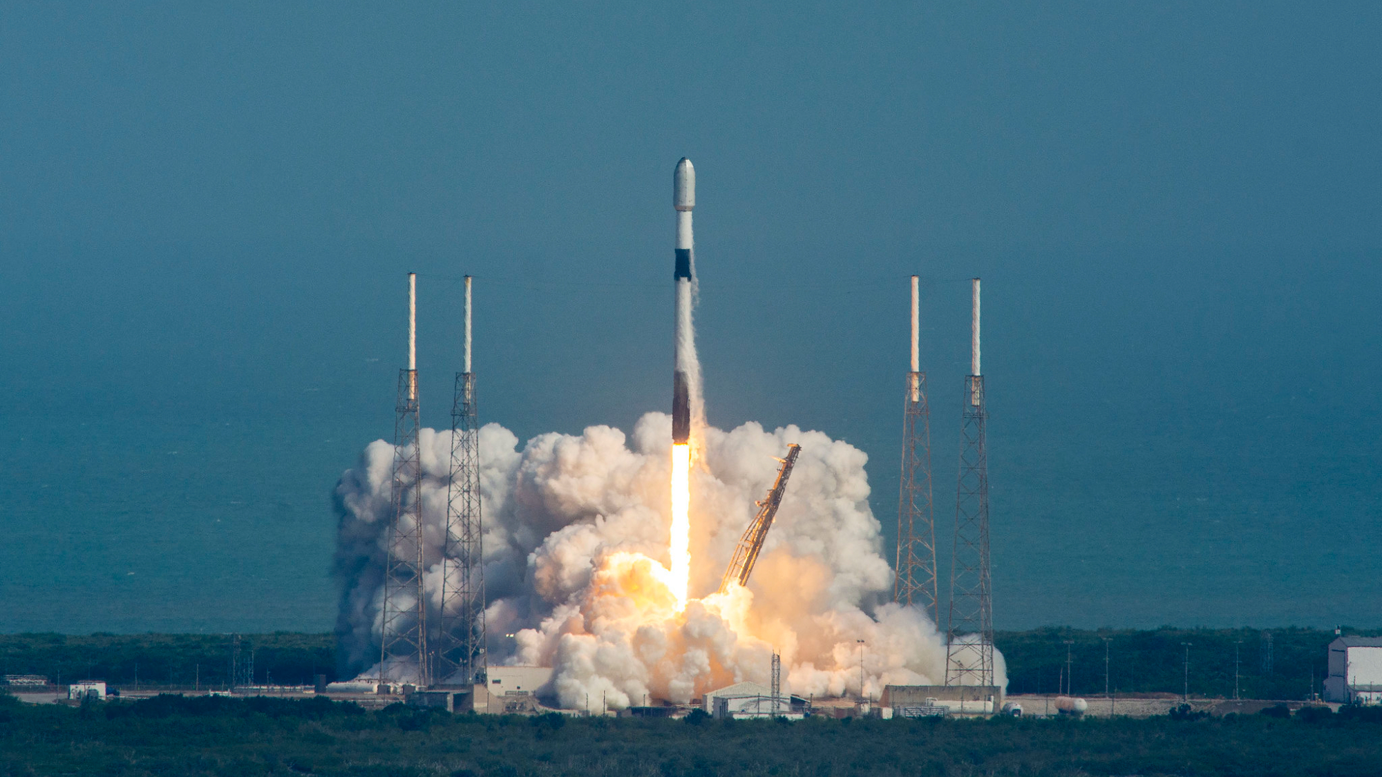 roket spacex falcon 9 hitam-putih diluncurkan ke langit biru.