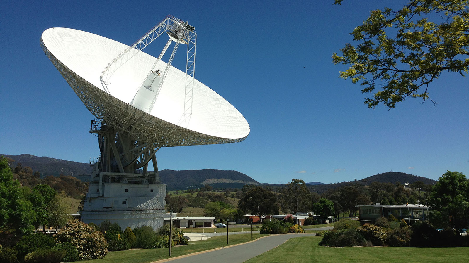 A giant satellite dish points toward the sky in a green landscape.